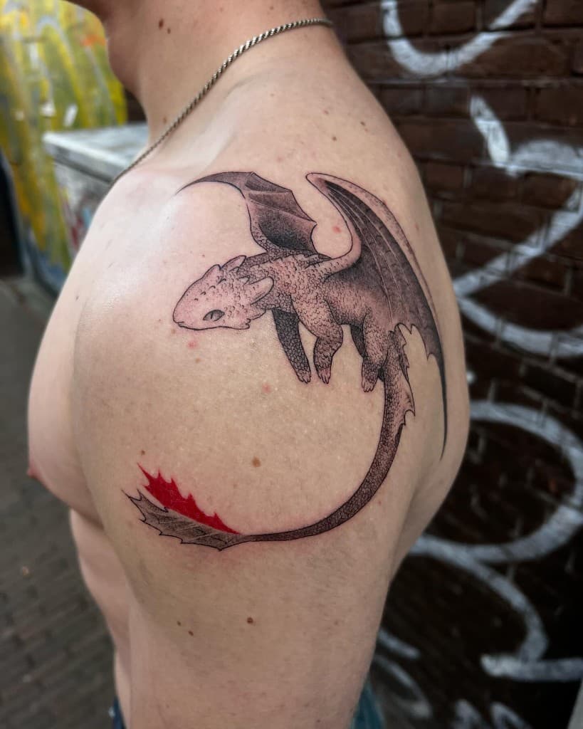 Black-and-grey stippled dragon tattoo on a shoulder, with a single red tail fin.